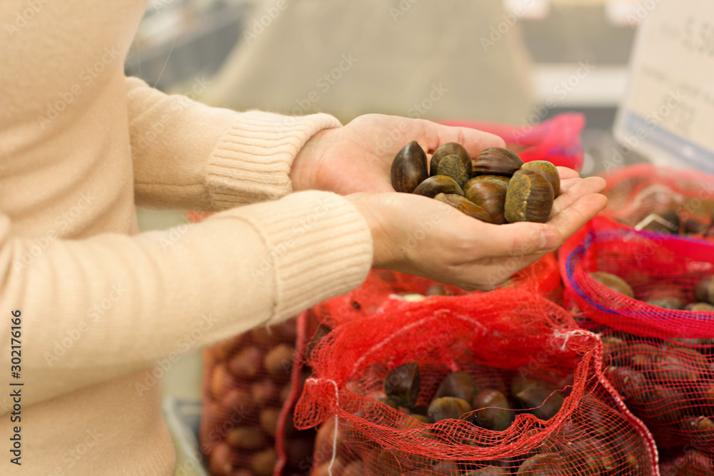Female hand choosing chestnuts in supermarket. Concept of healthy food, bio, vegetarian, diet.