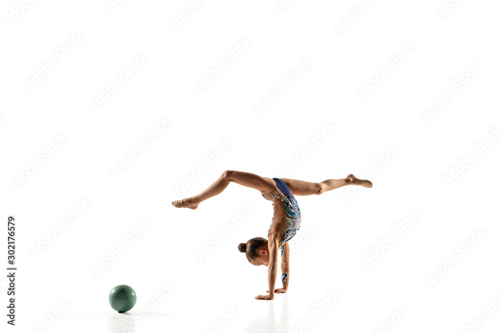 Little flexible girl isolated on white studio background. Little female model as a rhythmic gymnastics artist in bright leotard. Grace in motion, action and sport. Doing exercises with the ball.