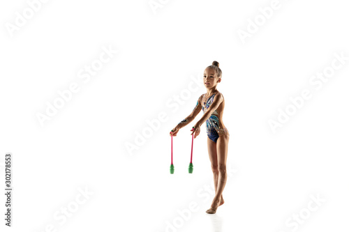 Little flexible girl isolated on white studio background. Little female model as a rhythmic gymnastics artist in bright leotard. Grace in motion, action and sport. Doing exercises with the maces.