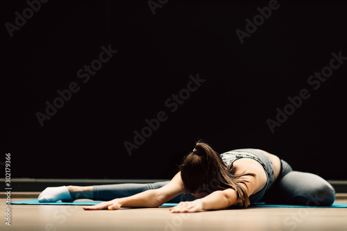 Athletic girl stretching lying on rug in sports hall