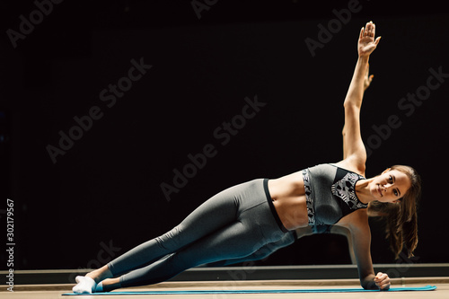 Fototapeta Naklejka Na Ścianę i Meble -  Young athlete woman on stretch in plank pose on rug in sports hall