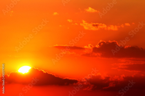 Red summer sun at sunset among the clouds.