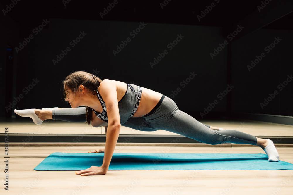 Sporty girl stretching sitting on blue rug on wooden floor