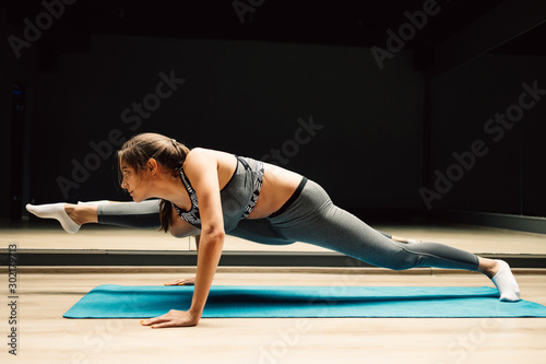 Sporty girl stretching sitting on blue rug on wooden floor