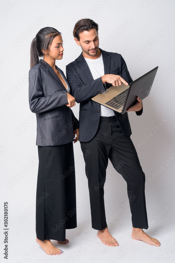 Full body shot of multi ethnic business couple using laptop together Full body shot of multi ethnic business couple using laptop together