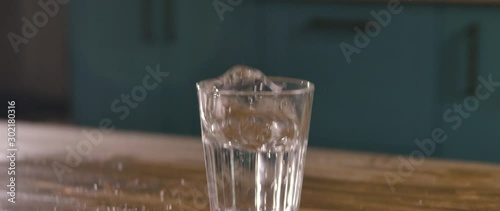 the wooden table shakes and tosses a clear glass of clear water.  the mug drops and the liquid spills. Water falling as a spray at a wet table. Drop the Hand Drink Mug