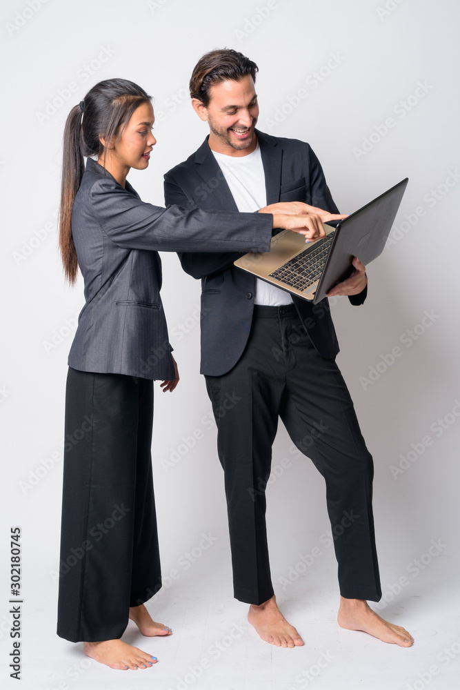 Full body shot of happy multi ethnic business couple working with laptop together Full body shot of happy multi ethnic business couple working with laptop together