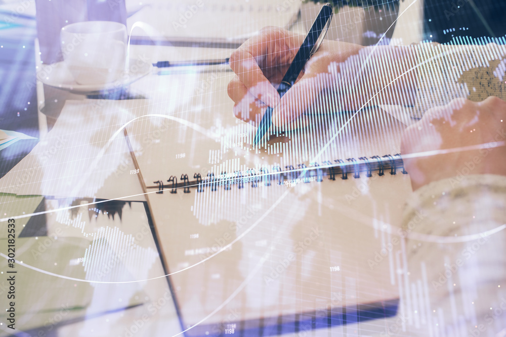 Forex chart hologram on hand taking notes background. Concept of analysis. Double exposure