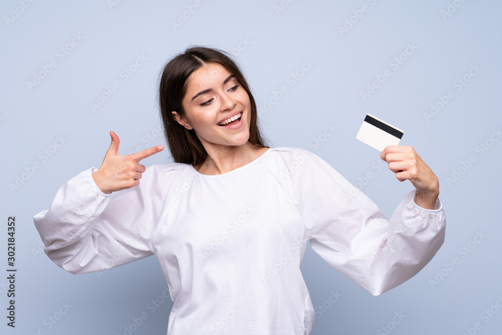 Young woman over isolated blue background holding a credit card Young woman over isolated blue background holding a credit card