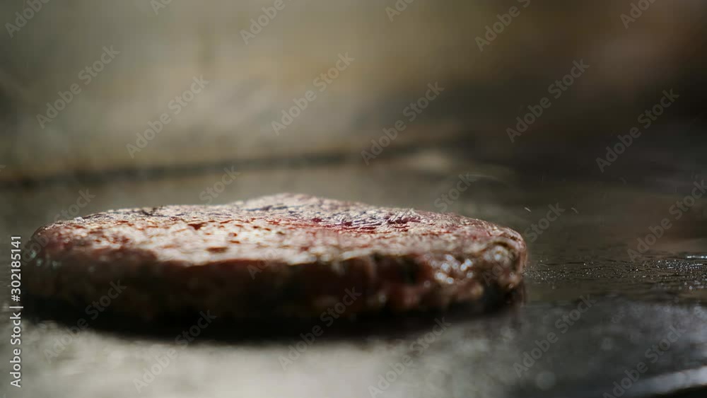 The cook puts a raw burger cutlet on an electric grill. The frying process begins The cook puts a raw burger cutlet on an electric grill. The frying process begins