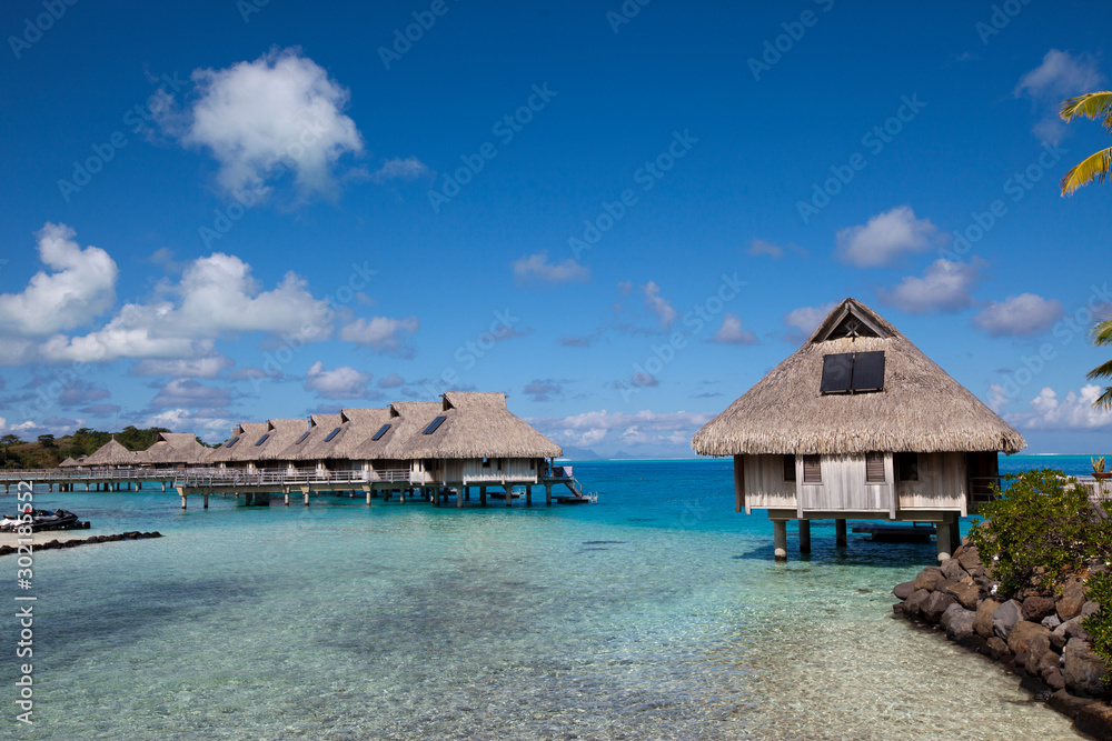 authentic traditional Polynesian houses with thatched roof above the water of the blue tropical sea