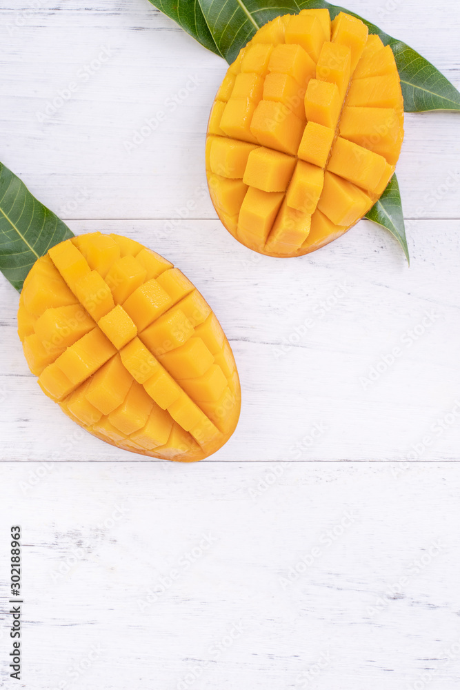 Beautiful chopped ripe mango with green leaves on bright white color wooden background, top view, flat lay, copy space. Tropical fruit design concept.