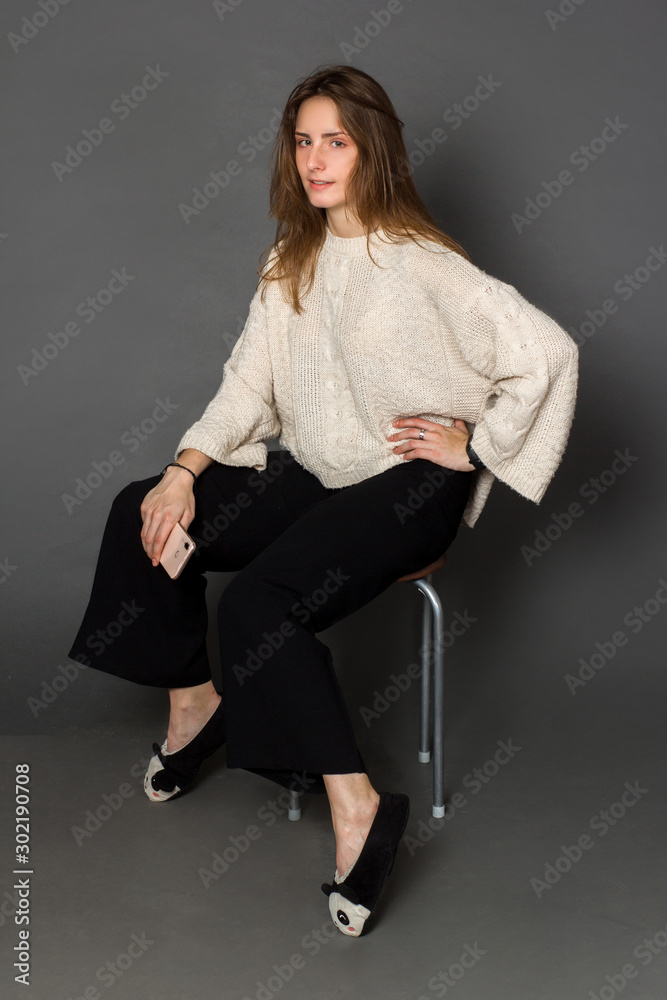 A girl in a light yellowish sweater and classic black trousers sitting on a chair and holding a mobile phone in his hand A girl in a light yellowish sweater and classic black trousers sitting on a chair and holding a mobile phone in his hand