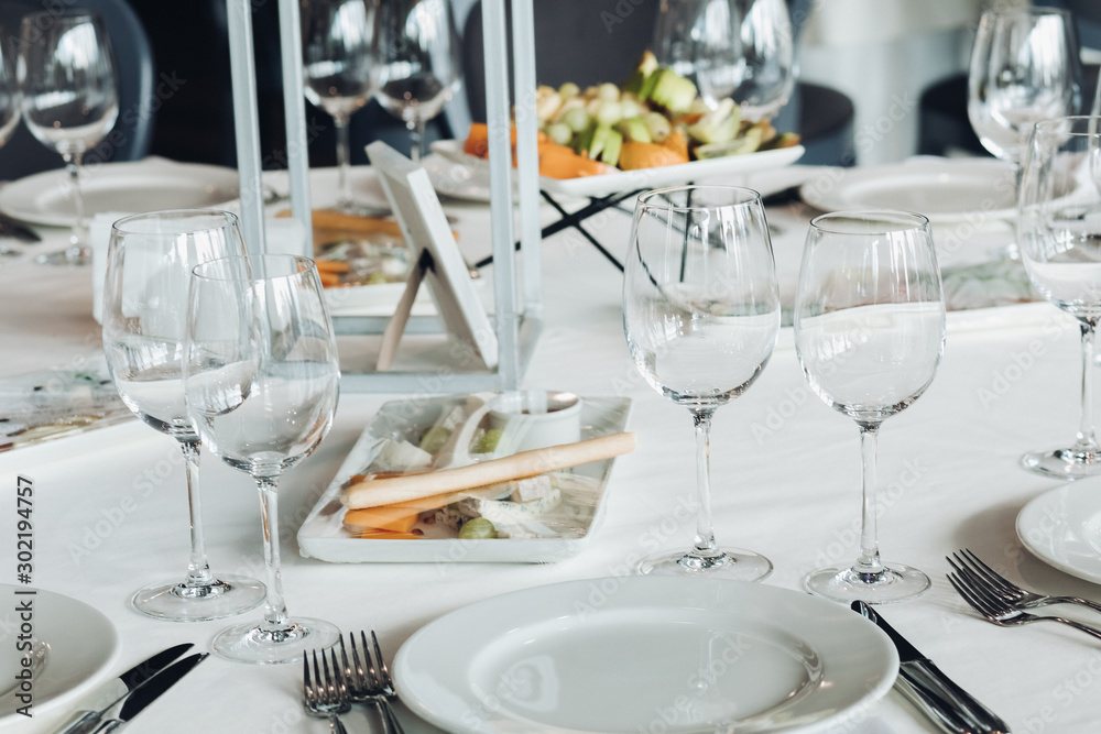 View over wedding table covered with white tablecloth with empty glasses, plates and utensils. Snacks are served on the table. View over wedding table covered with white tablecloth with empty glasses, plates and utensils. Snacks are served on the table.