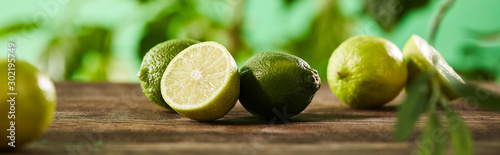 panoramic shot of cut and whole limes on wooden surface
