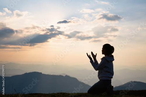 Tela Silhouette of a woman with hands raised in the sunset concept for religion, wors