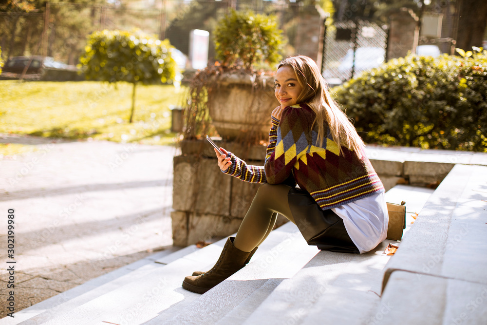 Young woman sitting on a stairs with mobile phone in autumn park