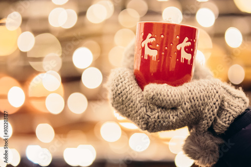 Christmas light and a woman holding in hand a red mug with hot drink photo