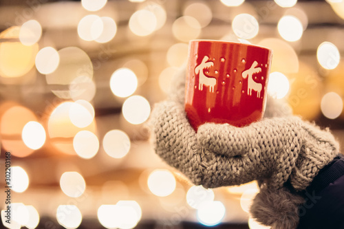 Christmas light and a woman holding in hand a red mug with hot drink photo