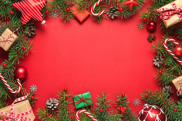 Christmas frame made of fir branches, gift boxes, red holiday decorations and candy on red background