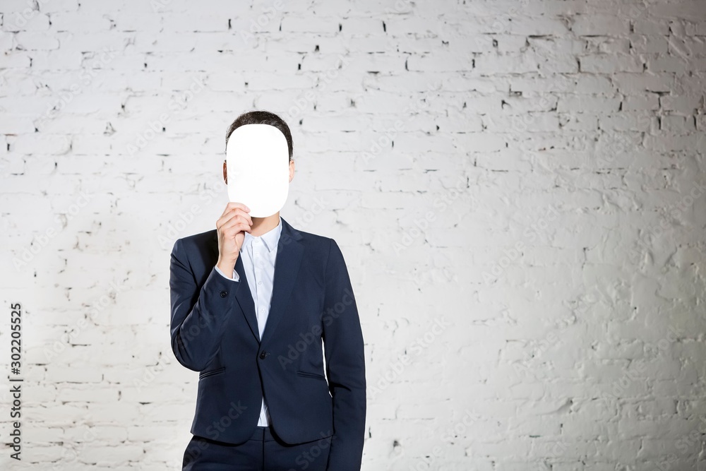 Young businesswoman covering face with blank paper against white brick wall at office Young businesswoman covering face with blank paper against white brick wall at office