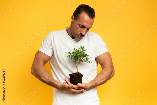 Boy cradles a small tree ready to be planted. yellow color background. concept of forestation, ecology and conservation photo