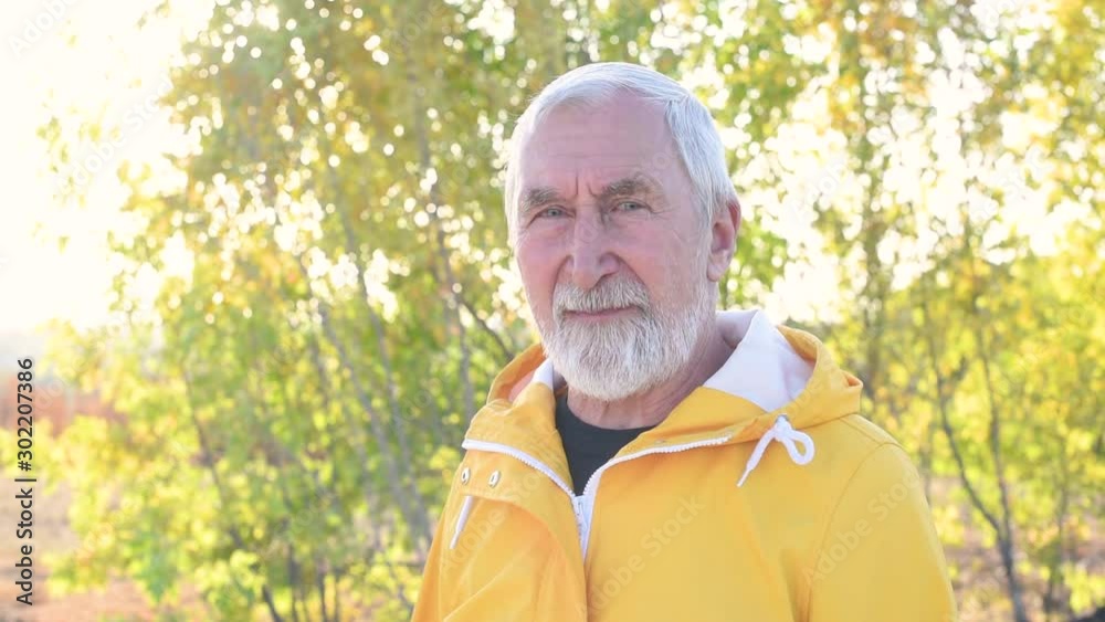 Elderly man with gray hair and beard in yellow raincoat at the sunset Elderly man with gray hair and beard in yellow raincoat at the sunset