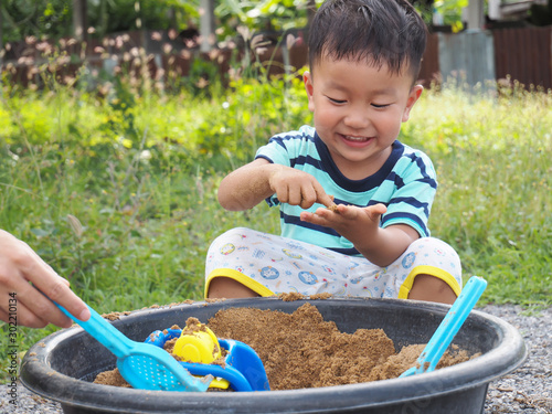 Asian cute child boy laughing with happy smiling face while playing sand with dad as natural meadow background with happy family time.