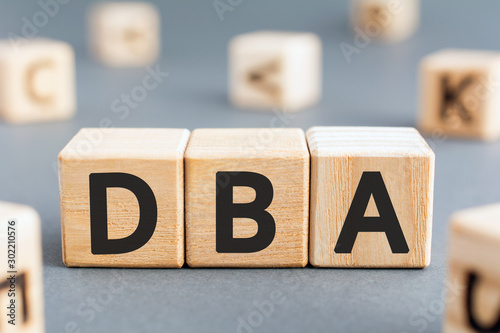 DBA - acronym from wooden blocks with letters, DataBase Administrator or doing business as abbreviation DBA concept, random letters around, gray background photo