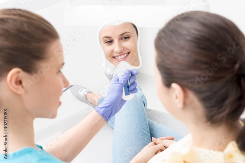 Dentist holding mirror while patient looking at her teeth in clinic