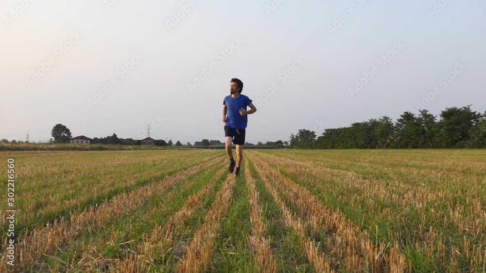 Slow motion of young sporty man runs in an agricultural field with shorts Slow motion of young sporty man runs in an agricultural field with shorts