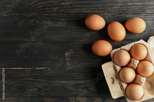 Chicken eggs in carton box on wooden background, space for text photo