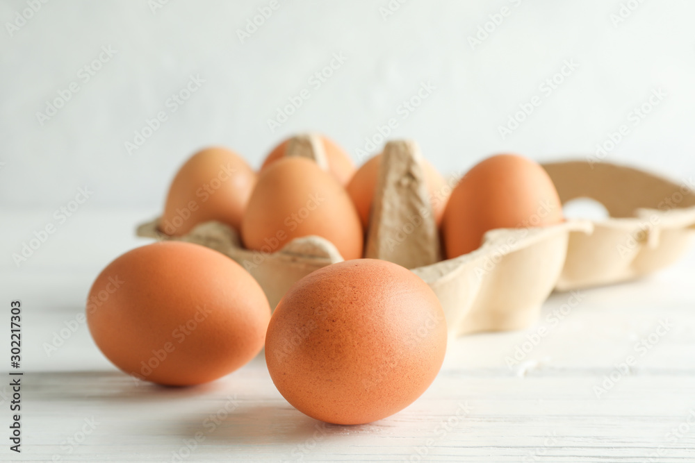 Chicken eggs in carton box on wooden table against white background Chicken eggs in carton box on wooden table against white background