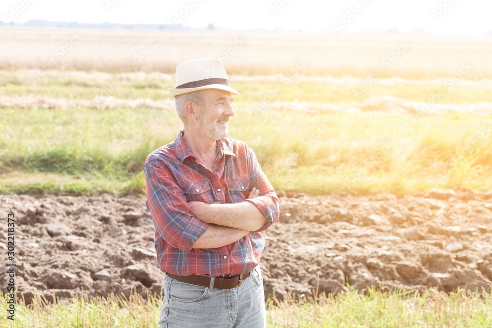 Senior farmer standing with arms crossed in field