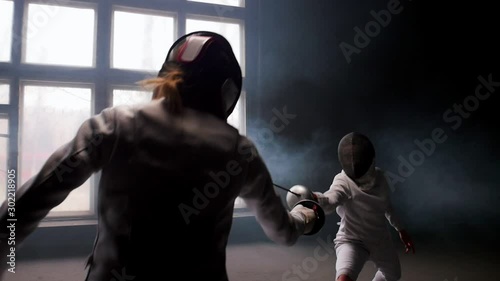 Two young women having a fencing duel in the smoky studio photo