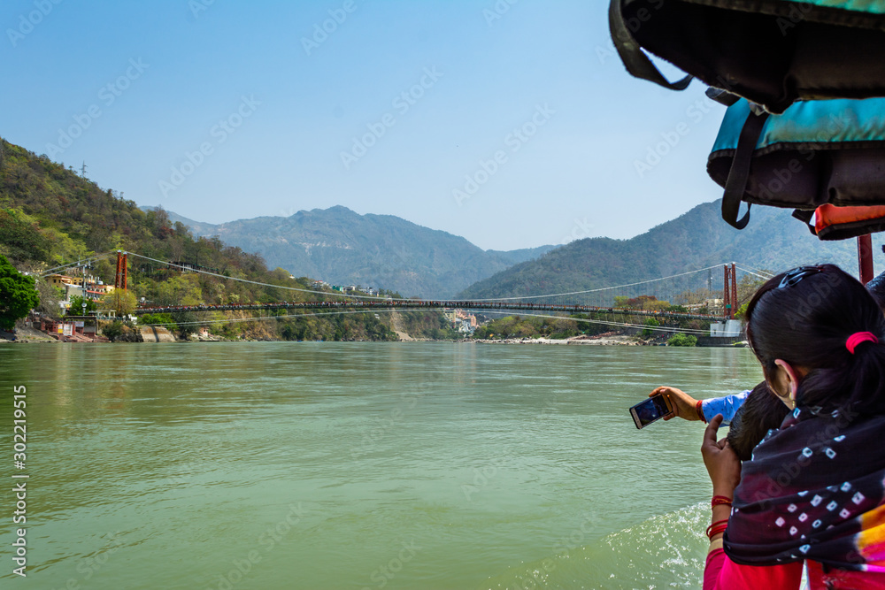 Woman taking picture of Ram Jhula bridge over Ganga River from a boat at Rishikesh. India