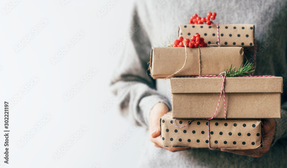 Elegant female hands holding gift boxes in plain brown paper decorated with red berries. Christmas concept. Copy space for text on a white background. - obrazy, fototapety, plakaty 