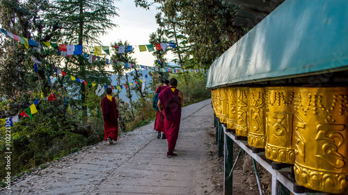 Photo Tibetan Monks walking among praying wheels, Dharamsala, India
