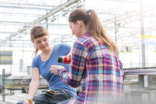 Female botanist pouring coffee for coworker in greenhouse