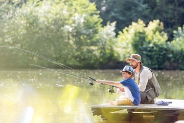 Father and son fishing in lake while sitting on pier