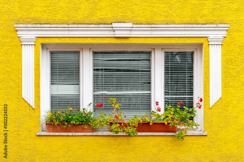 White window on a yellow wall. Facade of a residential building with decoration elements.