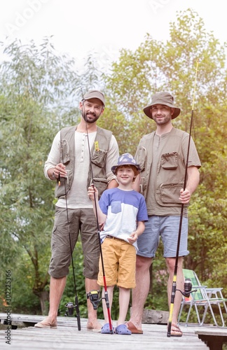 Full length portrait of smiling males standing with fishing rods on pier against trees © moodboard