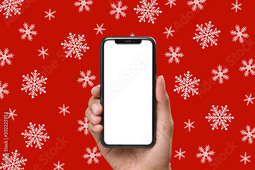 Hand holding the black smartphone with blank screen and modern frame less design on Christmas background of snowflakes in red colors photo