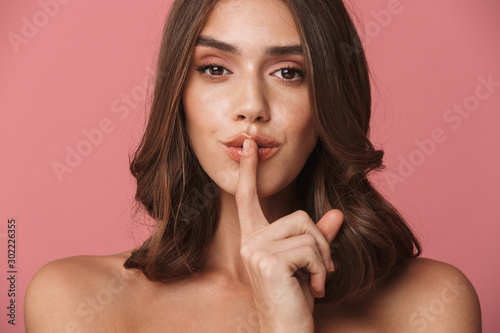 Portrait of happy young shirtless woman keeping finger at her mouth photo