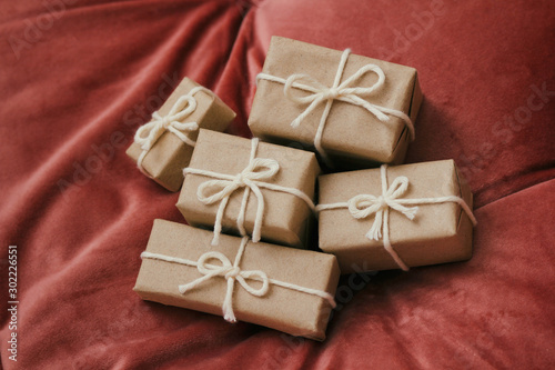 Presents for a Christmas. Gift boxes wrapped in craft paper and tie white string. Red velvet cloth background. Holiday mood.  © exienator