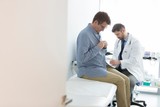 Doctor reading medical report while patient undressing for checkup at hospital