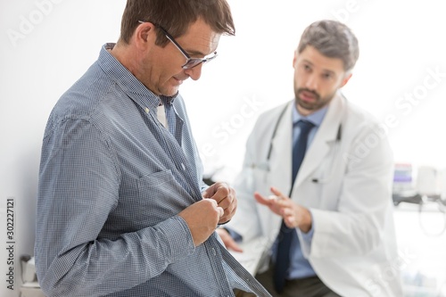 Doctor reading medical report while patient undressing for checkup at hospital © moodboard