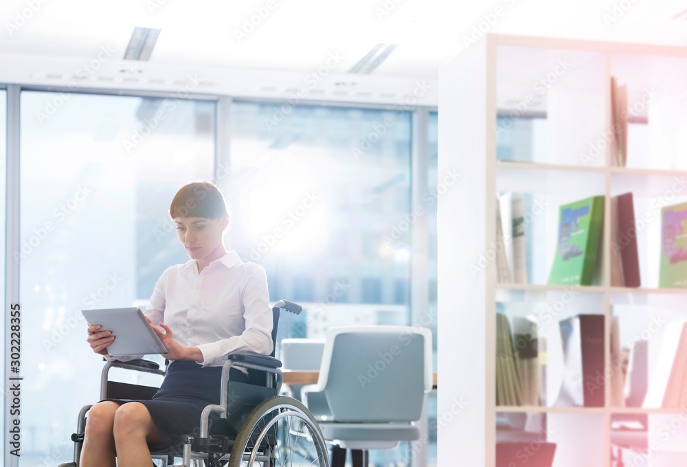 Businesswoman sitting in wheel chair while using digital tablet in office