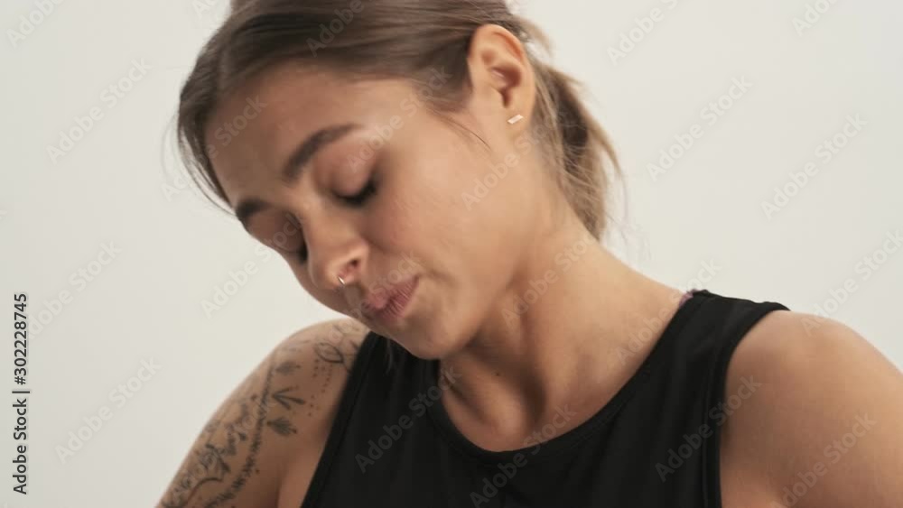 Wearied sporty woman wearing tracksuit touching her neck while turning her head isolated over white wall Wearied sporty woman wearing tracksuit touching her neck while turning her head isolated over white wall