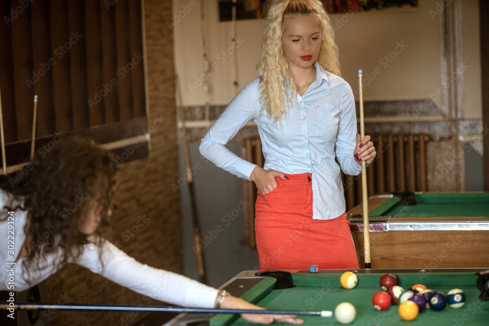 Obraz premium Beautiful smiling women playing billiards at a bar